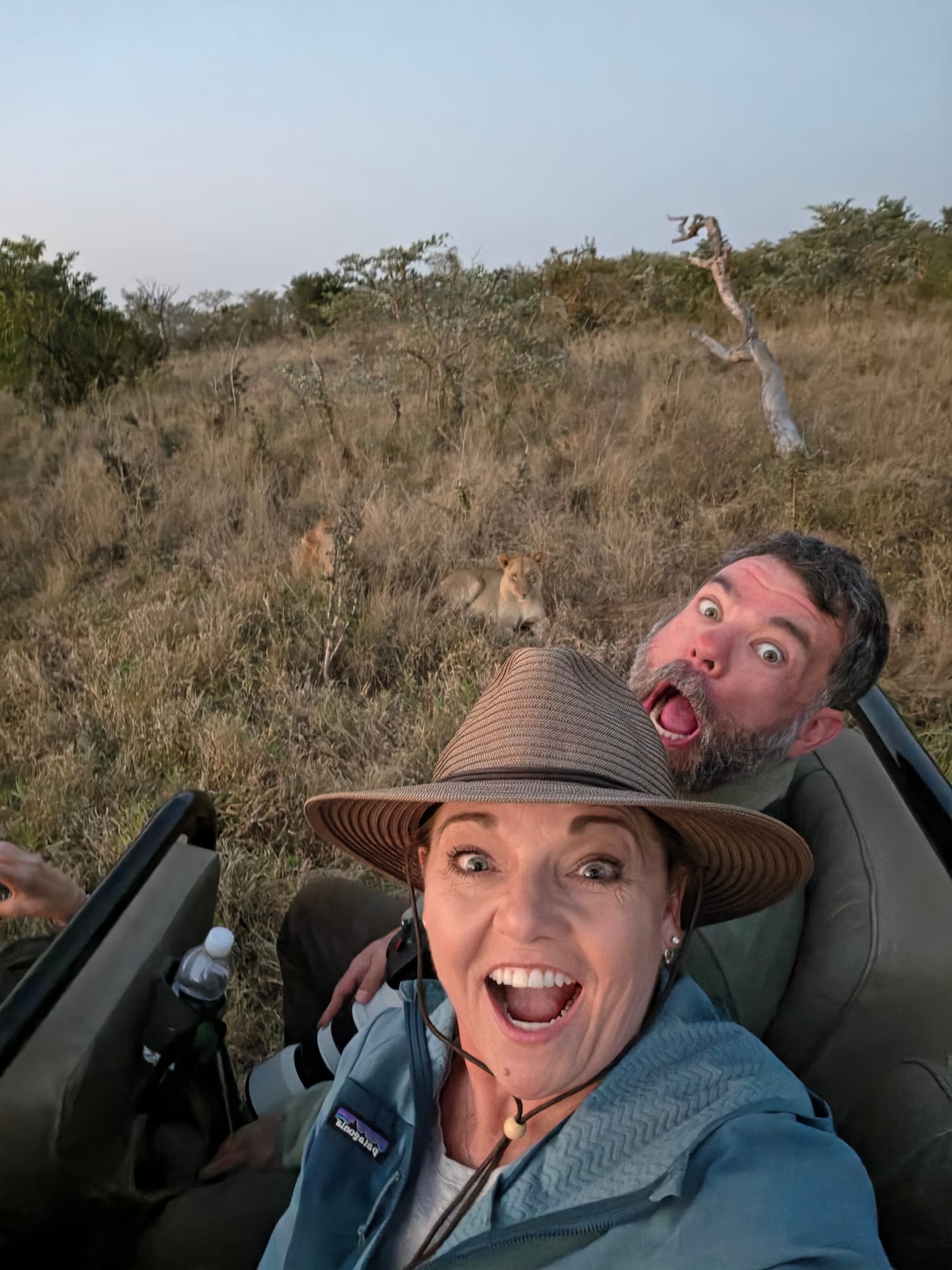 Tiffany Watt and a fellow traveler on a game drive with lions resting in the grass behind them