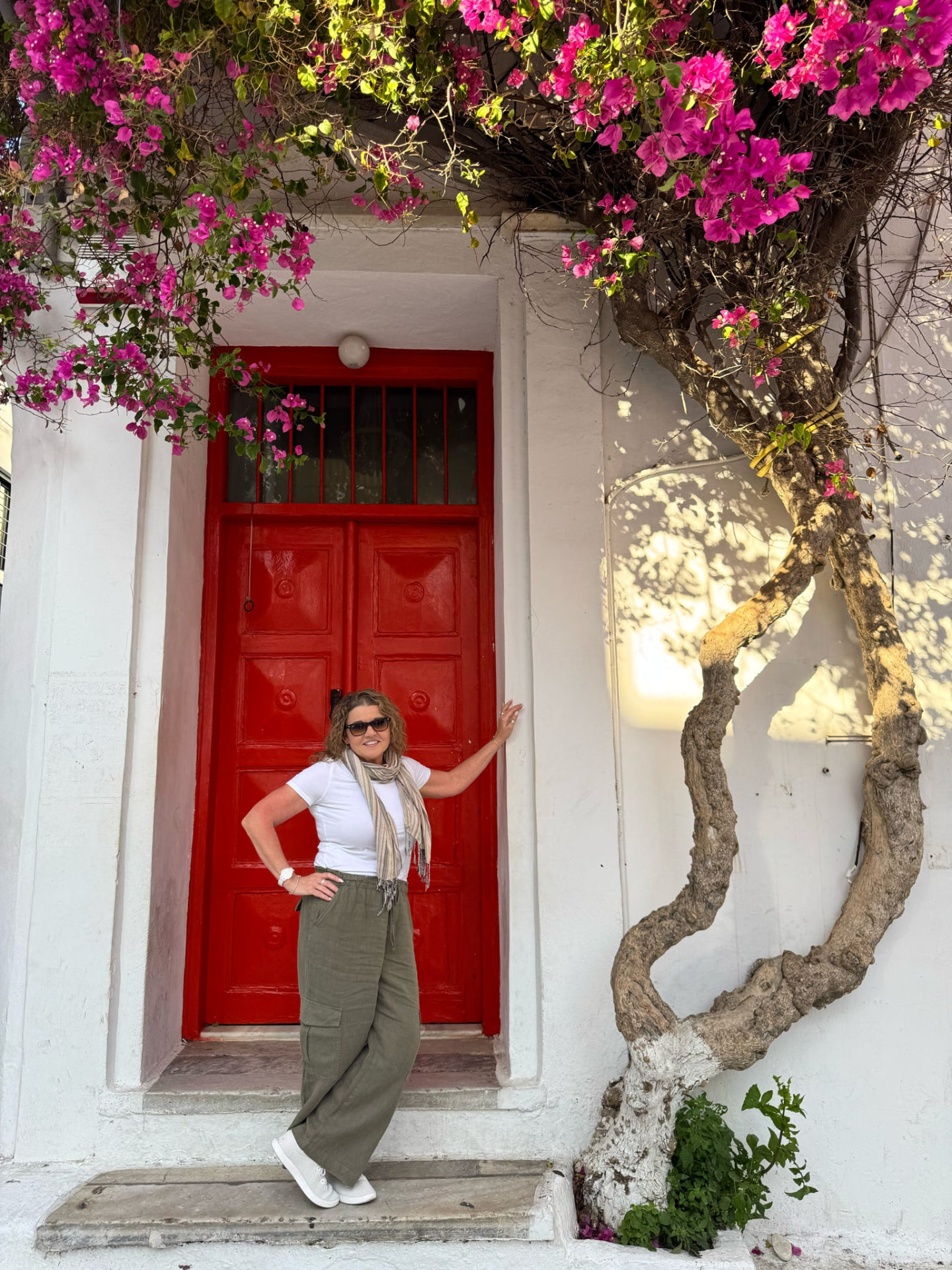 Tiffany Watt beside a red door framed by bougainvillea in a Greek island village