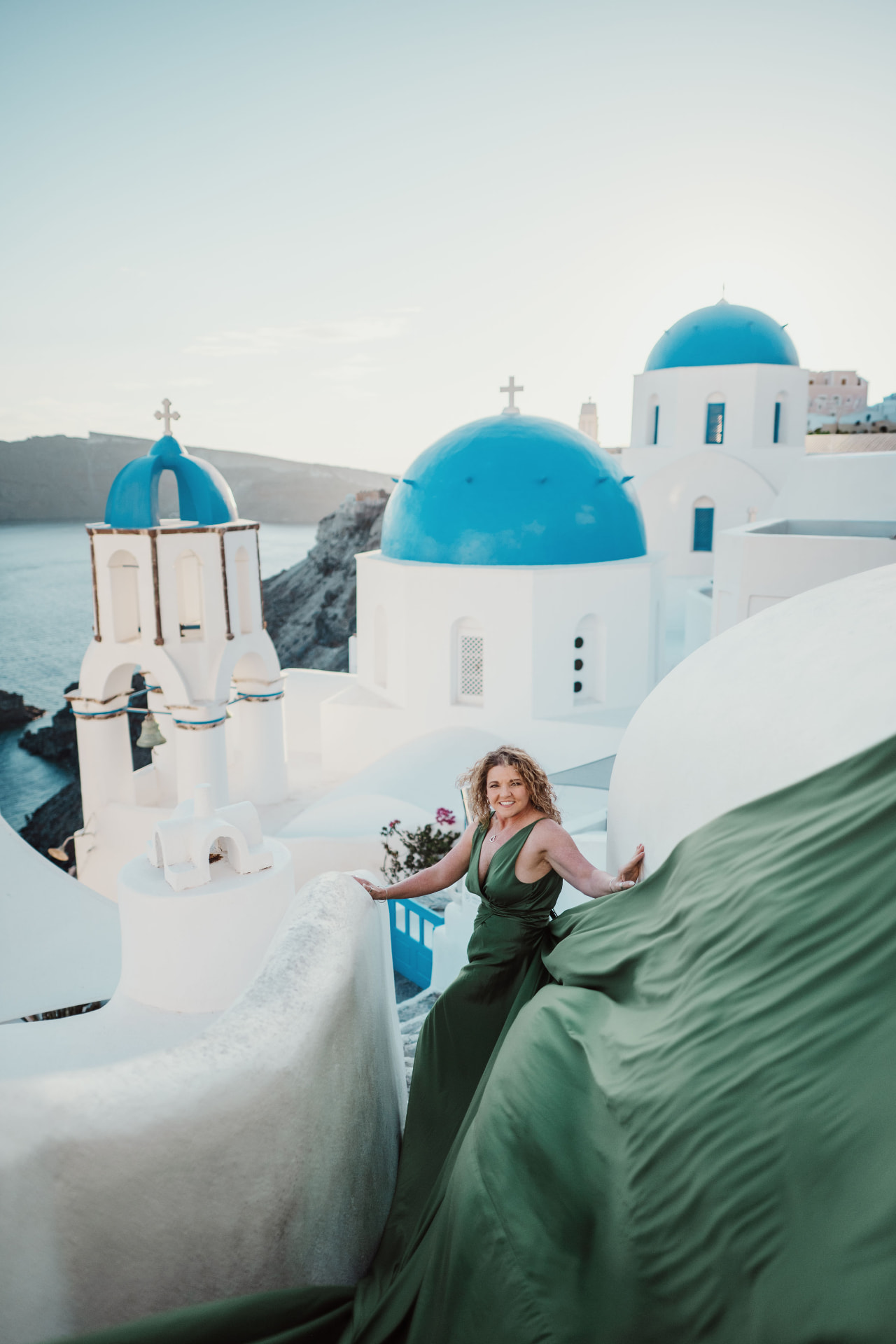 Tiffany Watt in a green flowing gown above the blue domes of Oia, Santorini, Greece