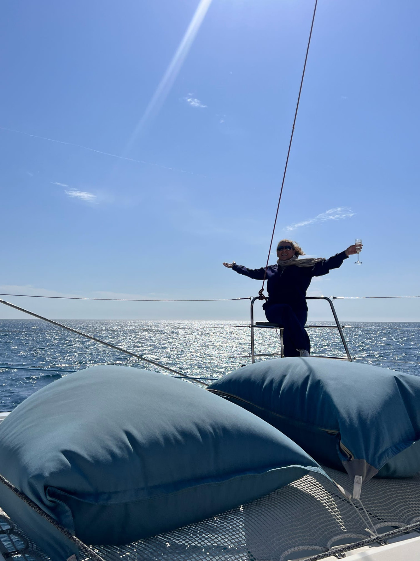Tiffany Watt with arms wide open at the bow of a catamaran under sail on the Mediterranean