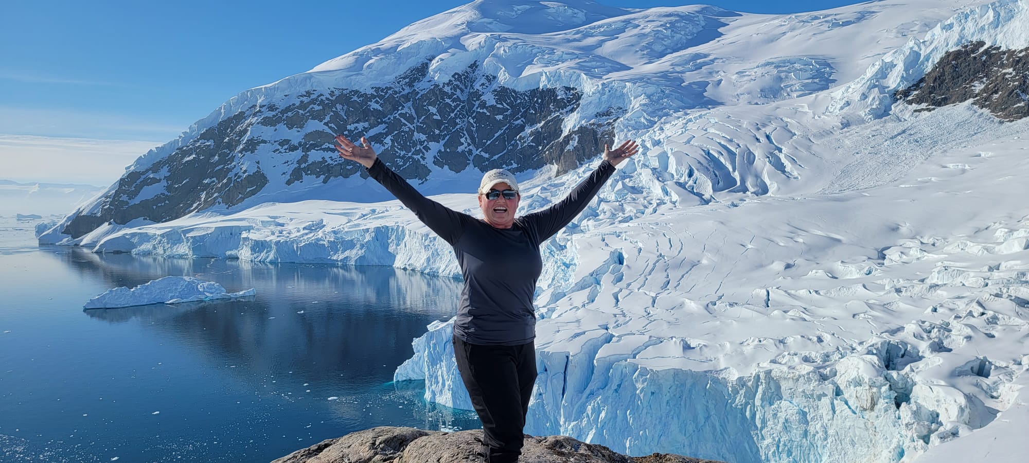 Tiffany Watt standing with arms raised on the shoreline at Neko Harbour, Antarctica