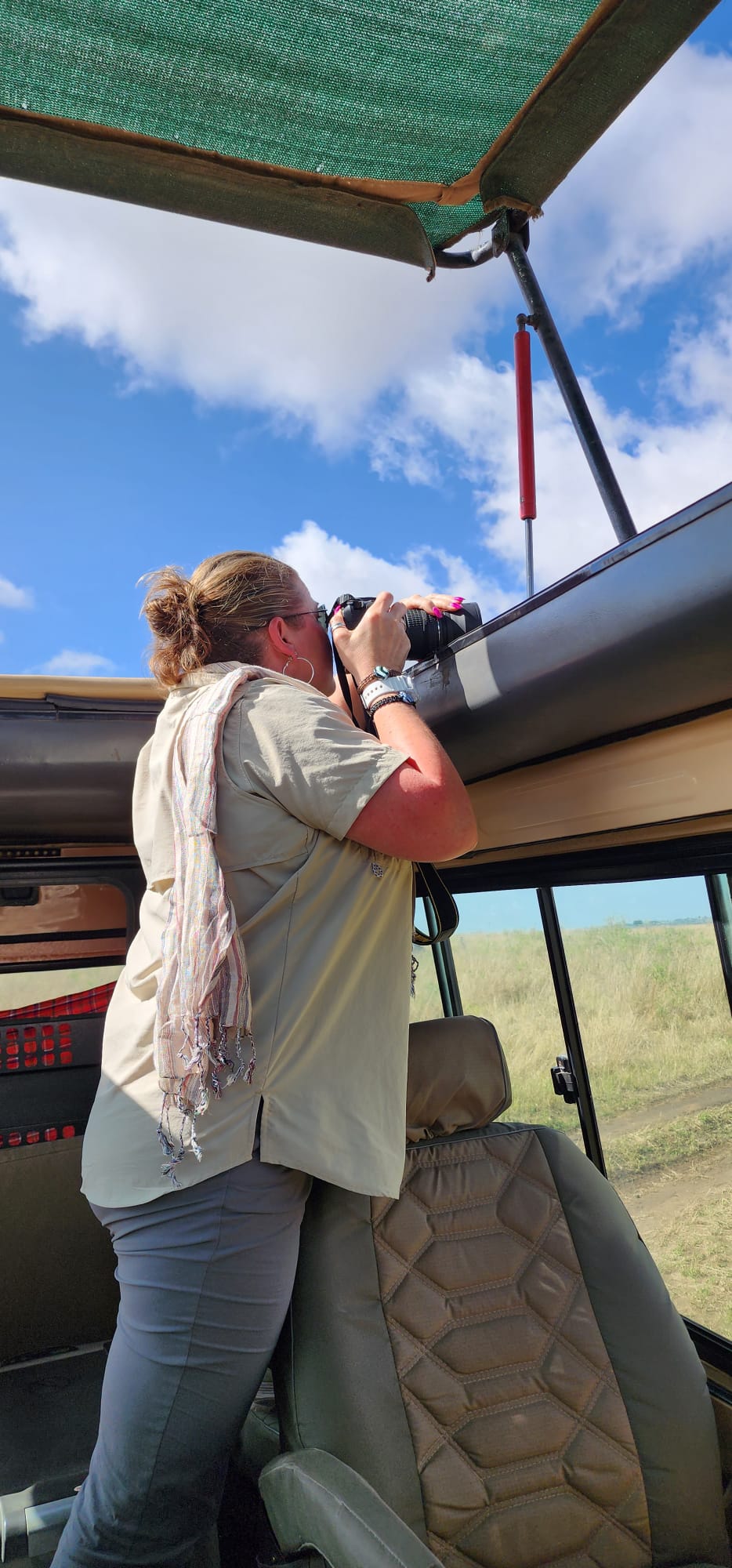 Tiffany Watt standing in a safari Land Cruiser photographing wildlife through the open roof hatch